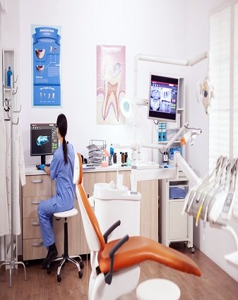 Stomatology office with modern equipment Stomatology office with modern equipment and nurse wearing blue uniform working on computer.